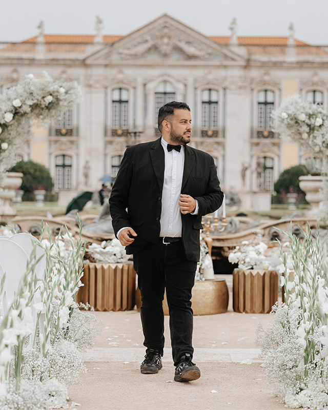 DJ Darman walking a white floral wedding aisle in front of a baroque palace facade