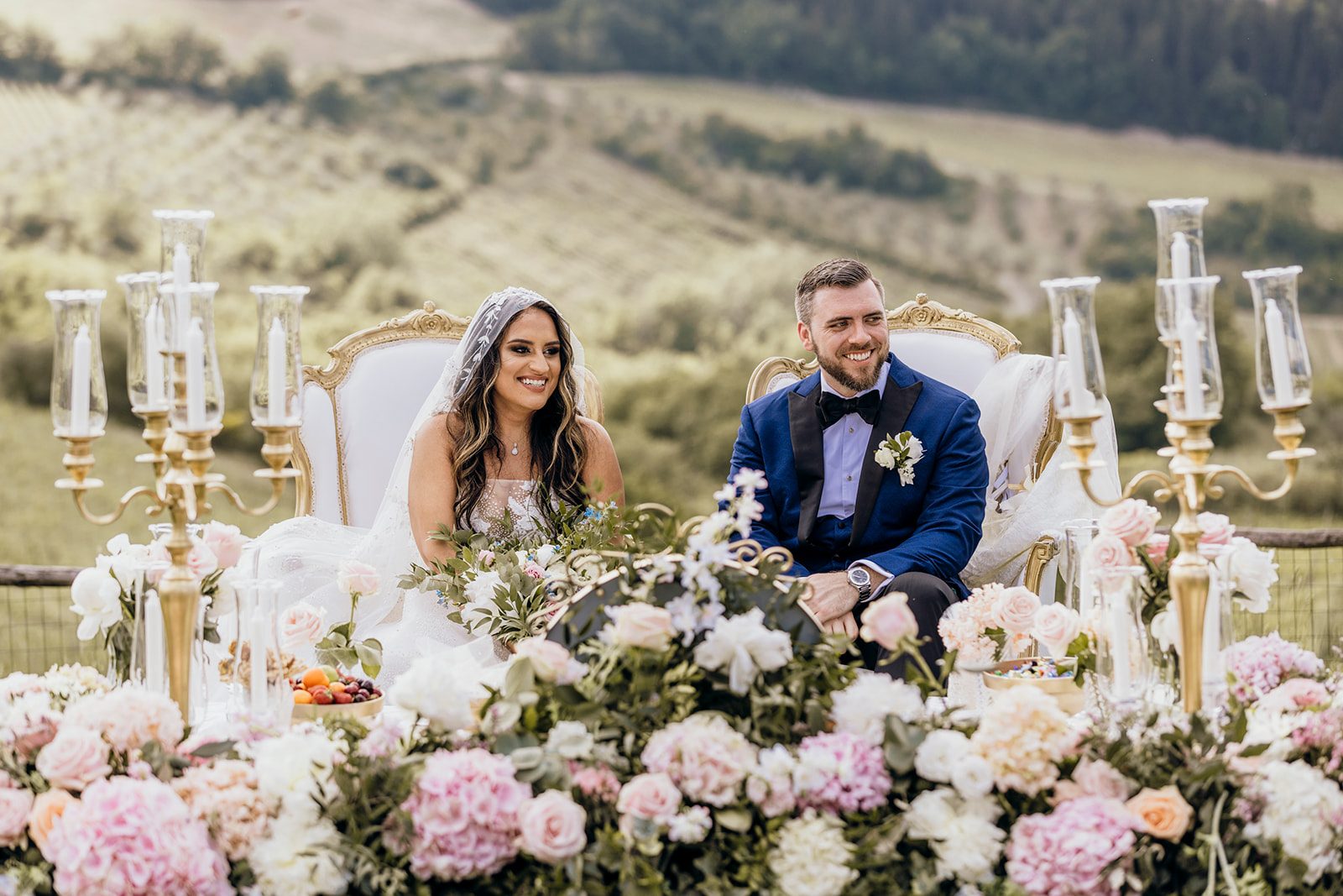 Couple seated at their aghd ceremony behind flowers and gold candelabra, above the vineyards of Tuscany