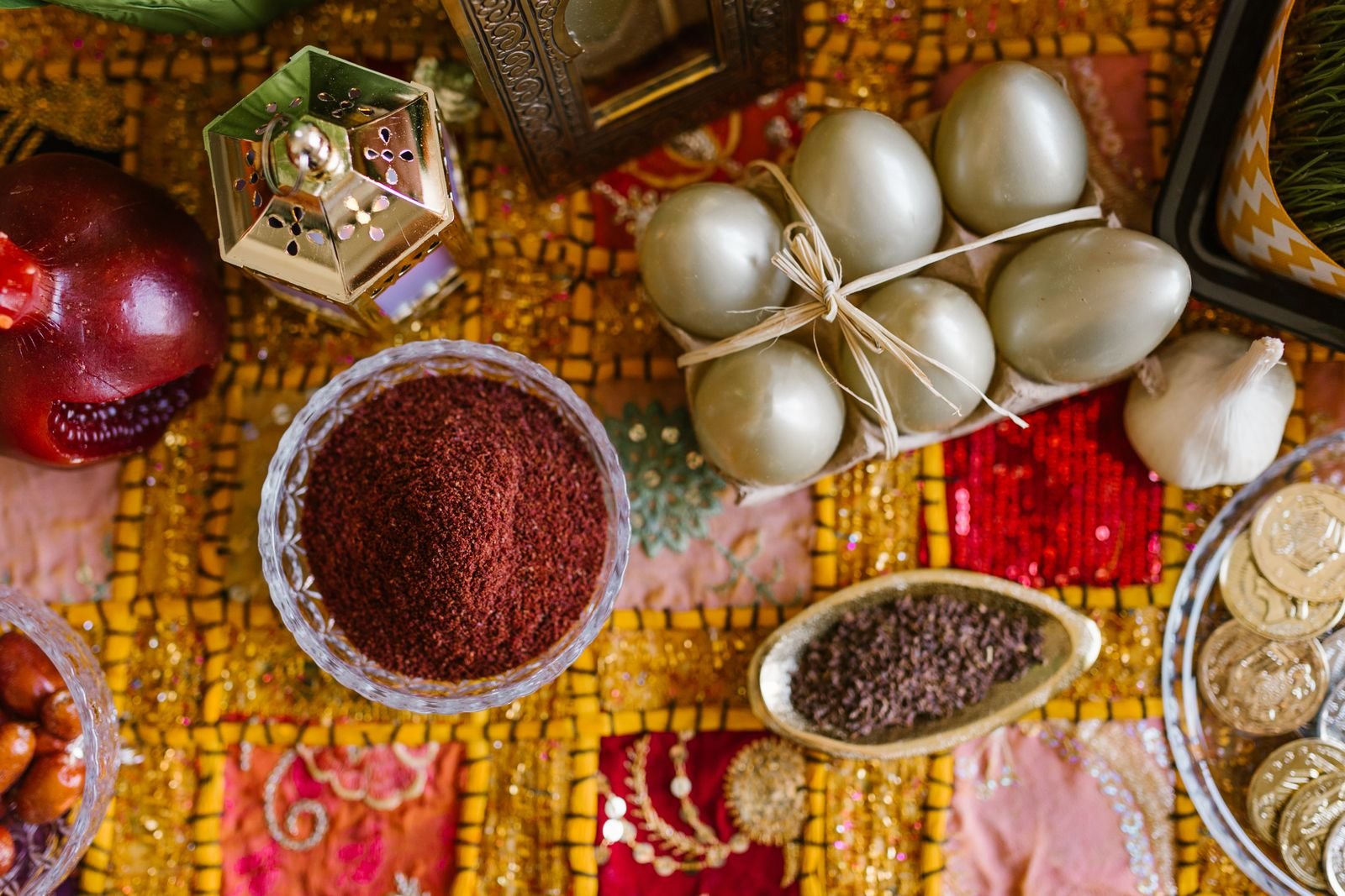 Traditional sofreh elements from above — sumac, painted eggs, pomegranate, sweets and gilded lanterns on embroidered patchwork textile