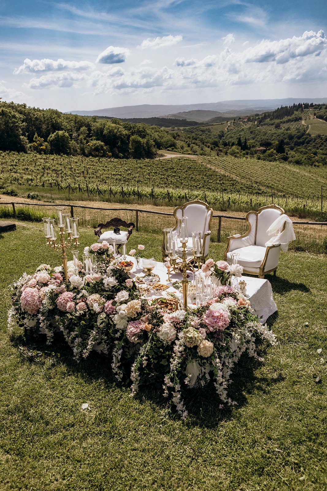 Sweetheart table covered in roses and hydrangeas above the vineyards of Tuscany, set for a destination wedding